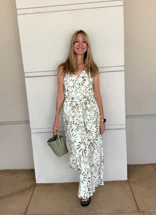 Woman in a white floral dress standing against a light-colored wall.