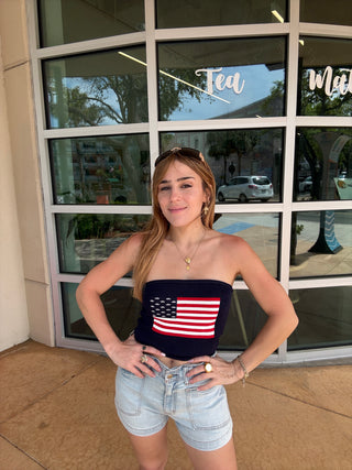 Woman wearing a tank top with an American flag design in front of a glass building.