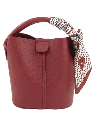A red pebbled leather bucket bag with a top handle and a patterned scarf tied to the handle, shown on a plain white background.