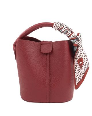 A pebbled leather bucket bag in deep burgundy red, featuring a matching top handle and a decorative patterned scarf tied to the side, shown against a plain white background.