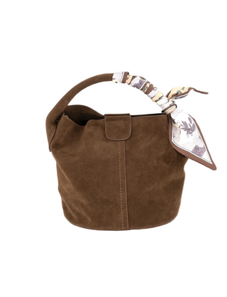 A brown suede bucket bag with a top handle, featuring a decorative scarf tied to the handle and a small hanging tag, shown against a plain white background.