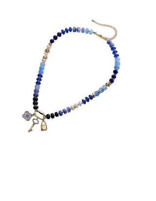 A collage showing a beaded necklace with colorful round beads, gold-tone chain, and small charms including a flower and key. The necklace is displayed on a light fabric background, with product details partially visible on the right side of the image.