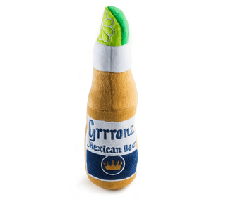 A plush dog toy shaped like a Corona Mexican Beer bottle, featuring a tan body, white neck, green lime detail, and a blue label with embroidered-style lettering.