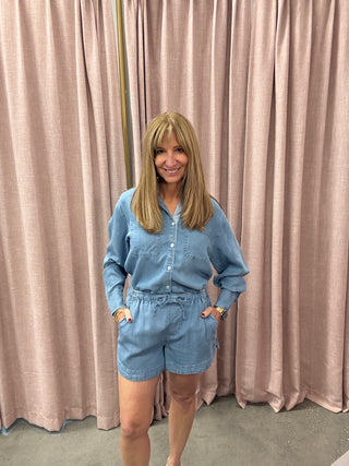 Woman wearing a blue outfit standing in front of pink curtains
