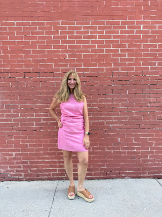 Woman in a pink dress standing against a red brick wall