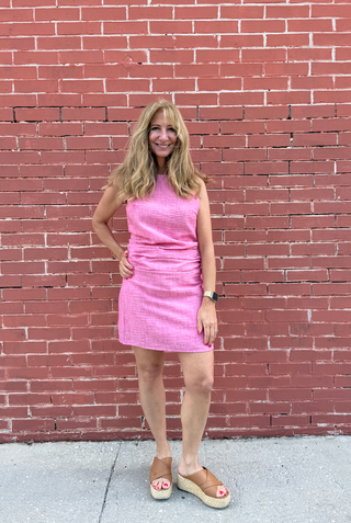 Woman in a pink dress standing against a red brick wall.