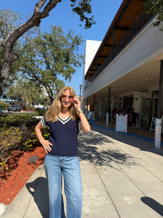 Woman standing on a sidewalk in front of a building with trees and a clear sky.