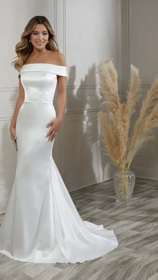 Woman wearing a white off-shoulder gown standing against a neutral background with decorative elements.