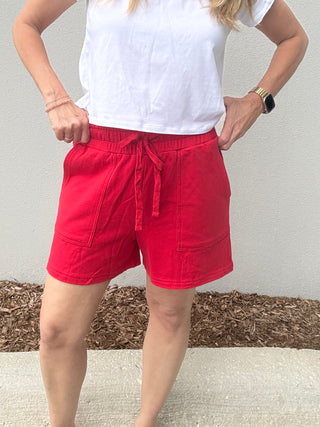 Person wearing red shorts and a white top against a neutral background