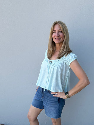 Woman wearing a light blue top and denim shorts against a plain background