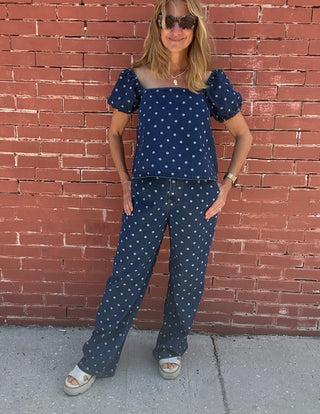 Woman wearing a navy blue outfit with white polka dots against a red brick wall.