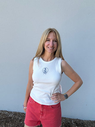 Woman wearing a white sleeveless shirt with a logo and red shorts against a light blue wall.