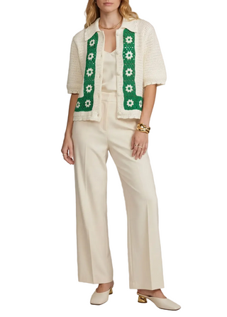 Woman wearing a cream outfit with a green floral-patterned cardigan against a neutral background