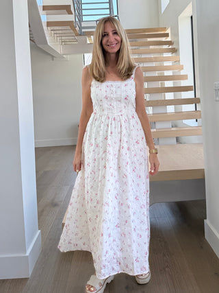 Woman in a white floral dress standing in a modern indoor setting with wooden stairs.