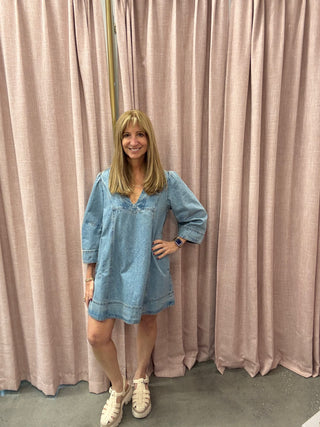 Woman in a blue dress standing in front of pink curtains