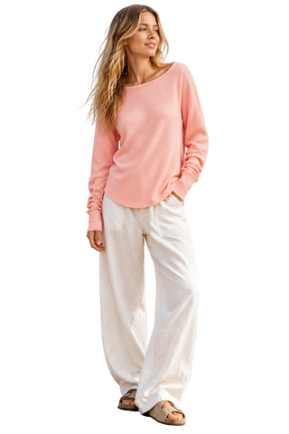 Woman wearing a pink sweater and brown pants with a plain background