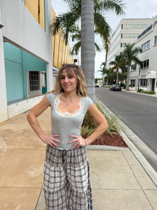 Woman standing on a sidewalk with palm trees and buildings in the background wearing a Free People Oh My Darling Tee / Heather Grey with lace around the neckline