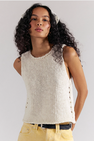 Woman wearing a sleeveless knitted top with buttons on a plain background