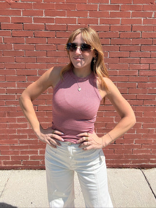 Woman wearing a pink top and white pants standing against a red brick wall.