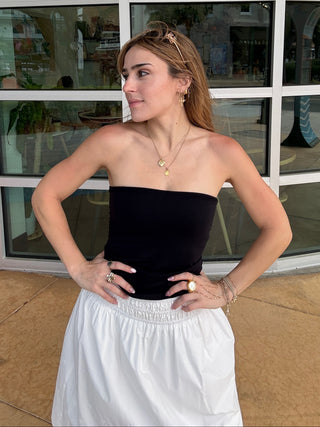 Woman in a black top and white skirt standing in front of a glass window.