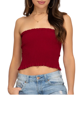 Woman wearing a red strapless top and blue jeans on a plain background