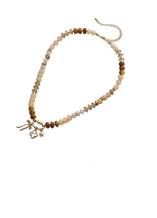 A split-screen product collage showing two beaded necklaces on a beige textured fabric background. The top necklace features beige, brown, and white beads with a gold bow charm and gold-tone chain.