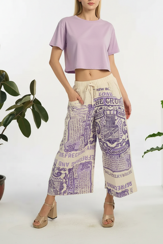 Woman wearing a graphic t-shirt and patterned pants with plants in the background