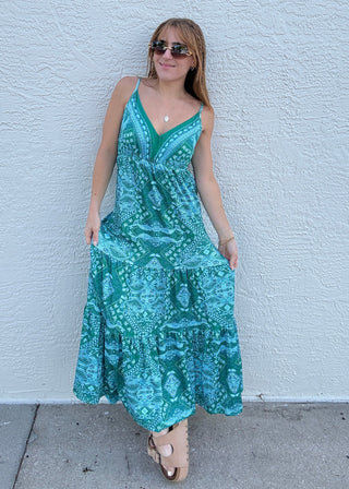 Woman in a green patterned dress standing against a light blue wall.