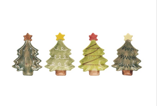 Four small ceramic Christmas tree ornaments in assorted green shades, each topped with a star in a different color, arranged in a row on a plain white background.