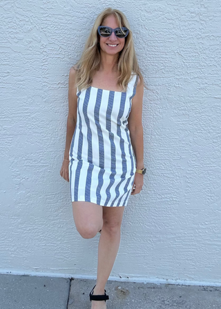 woman standing in a blue and white striped dress in front of a grey wall background