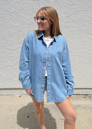 Person wearing a blue striped shirt standing on a sidewalk.