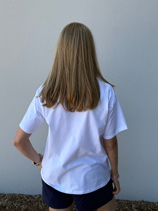 Person wearing a white t-shirt and dark shorts standing against a plain wall.