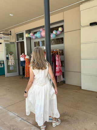 Woman in a white dress walking towards a store entrance with colorful balloons.