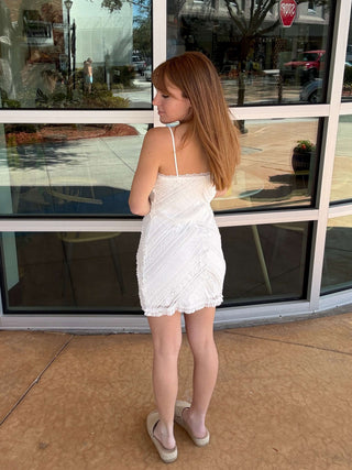 girl in a white dress standing outside a store with large glass windows.