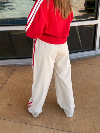 Person wearing a red jacket and white pants standing in front of a store window.