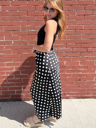 Woman in a polka dot dress standing on a red brick sidewalk.