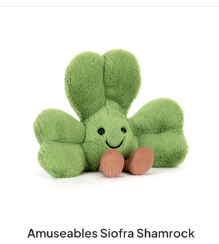 Green plush shamrock toy with a smiling face on a white background