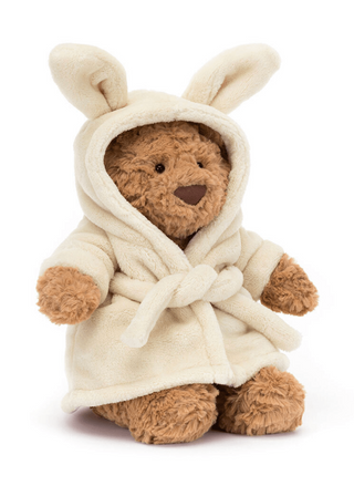 Stuffed teddy bear wearing a white robe with bunny ears on a white background
