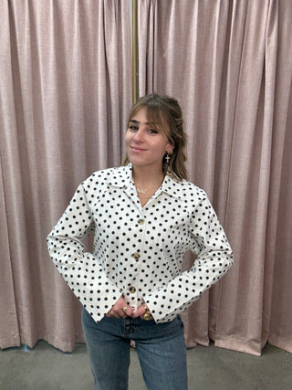 Person wearing a polka dot blouse standing against a curtain.