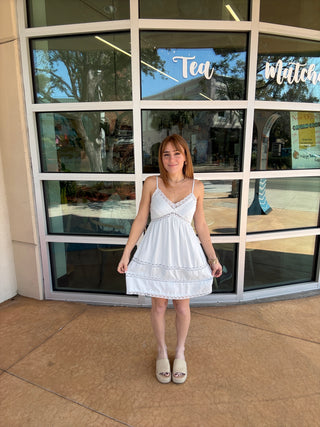 Person in a white dress standing in front of a glass door with reflections.