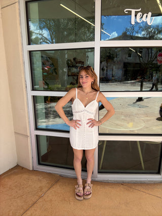 Woman in a white dress standing in front of a glass door with reflections.