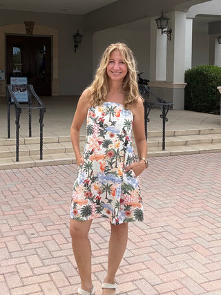 Woman in a floral dress standing on a brick patio in front of a building entrance.