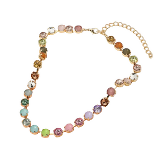 A gold-tone chain necklace with a series of round, multicolored faux gemstones in rose gold-toned settings, displayed on a white ceramic plate over a soft peach background.