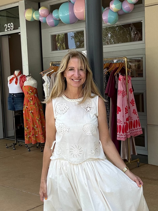 Woman in a white dress standing in front of a store with clothing displays.