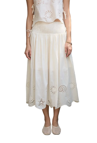 Woman wearing a white embroidered top and beige skirt on a white background