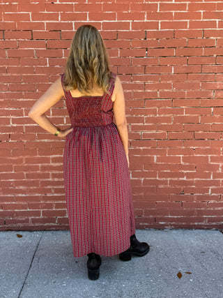 Person wearing a red checkered dress standing on a brick sidewalk.