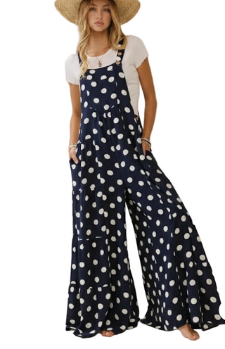 Woman wearing a navy blue polka dot jumpsuit on a plain background