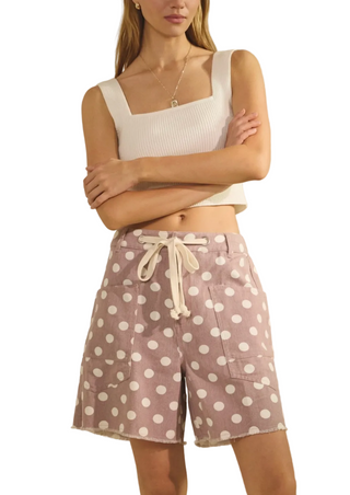 Woman wearing a white sleeveless top and polka dot shorts against a neutral background