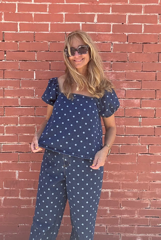 Woman wearing a navy blue top and pants with white polka dots against a red brick wall.