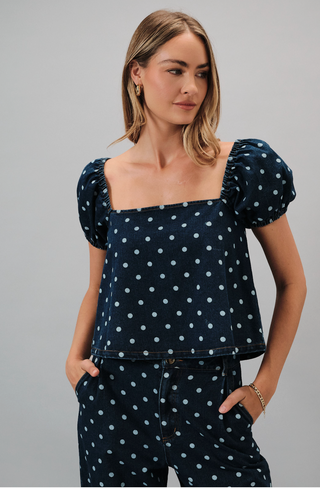 Woman wearing a navy polka dot top and pants against a gray background